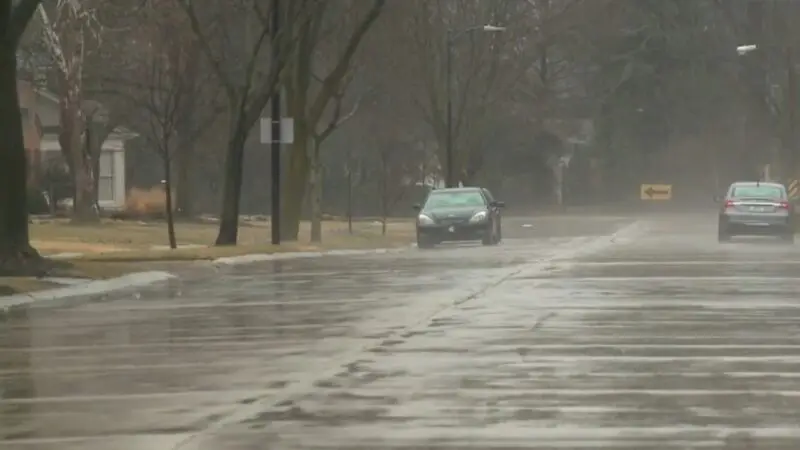 A Rainy Day in Fort Wayne with Cars Driving on A Wet Street Lined with Trees and Homes in The Background