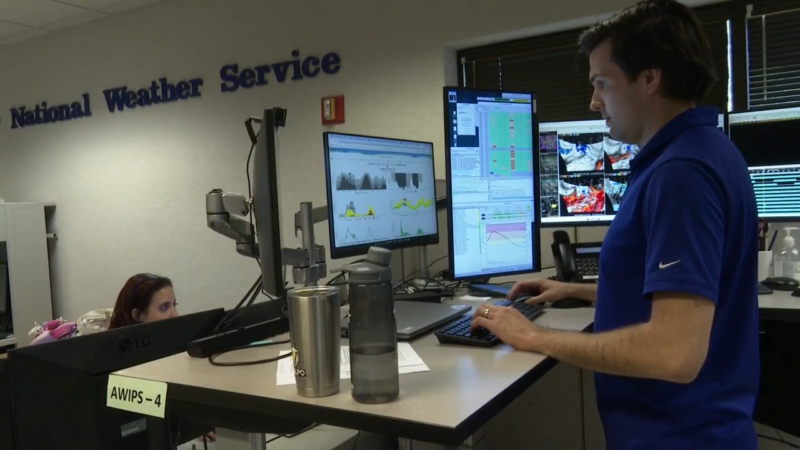 The Image Shows a Meteorologist Working at A Desk with Multiple Computer Monitors, Gathering and Analyzing Weather Data at A National Weather Service Office