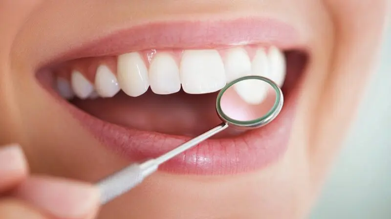 Close-up of a bright smile with white teeth and a dental mirror held near the mouth