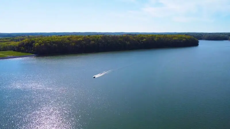 A boat speeding across the calm waters of Monroe Lake, surrounded by a lush green forest on a sunny day